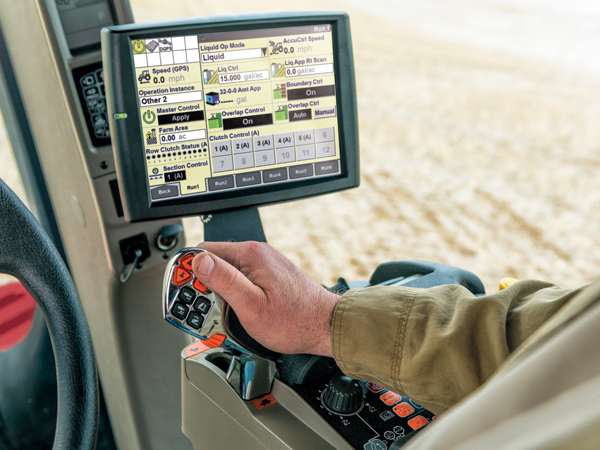 A person operating a remote inside a tractor cab with a screen displaying various functions …