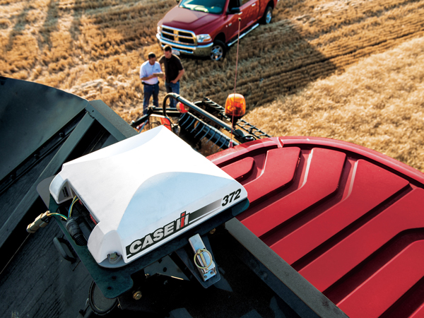 Two people standing in a large field near a truck and a building with a Case IH receiver on the …